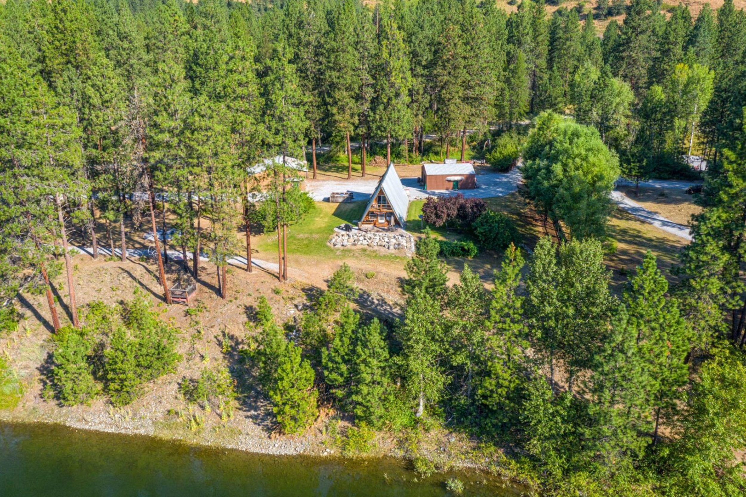 A-frame cabin surrounded by forest and river.